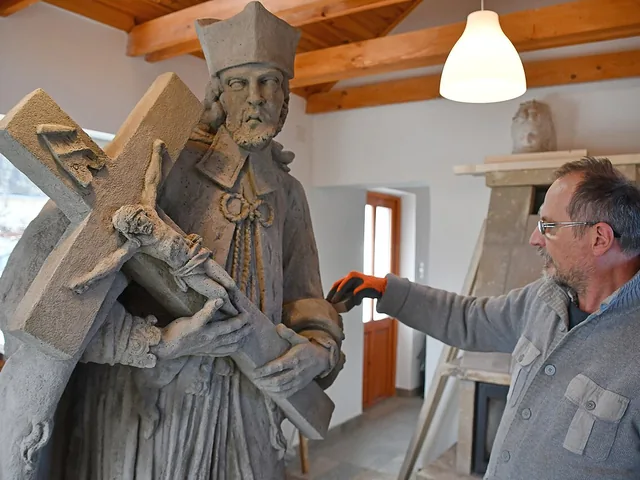 Restaurátor egy barokk kőszobor sérült részleteit vizsgálja a műhelyben